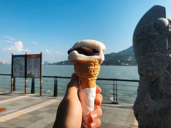 Cropped hand having ice cream cone on promenade against blue sky