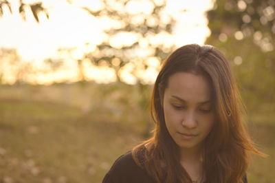 Young woman thoughtful and slightly looking at ground with beautiful bokeh in golden hour