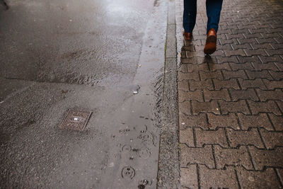Low section of man walking on wet footpath