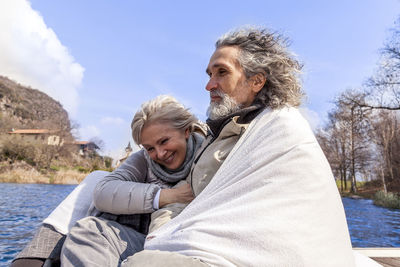 Happy senior couple sitting on shore against sky