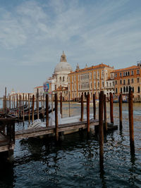 Wooden posts in canal against sky