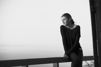 Young woman looking away while standing by railing against sky