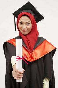 Young woman in graduation gown standing against white background