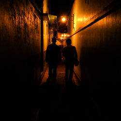 Rear view of silhouette man walking on illuminated street at night