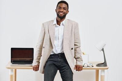 Portrait of young man using laptop while sitting against white background
