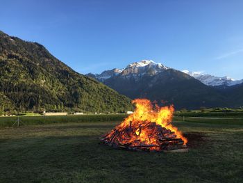 Burning firewood on field against blue sky