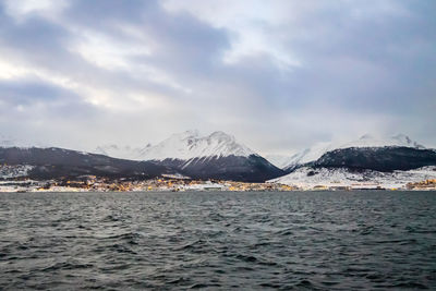 Scenic view of sea by snowcapped mountains against sky