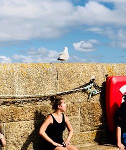 Woman sitting by seagulls against sky