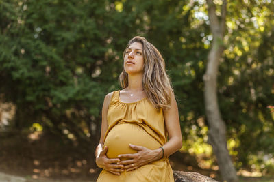 Pregnant woman looking away while standing against trees