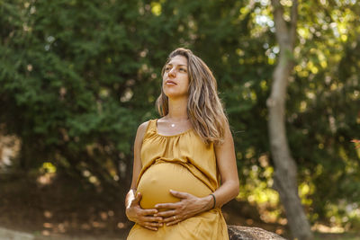 Young woman looking away while standing against trees