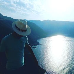 Man looking at sea by mountain against sky