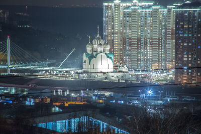 Illuminated bridge over river by buildings in city at night