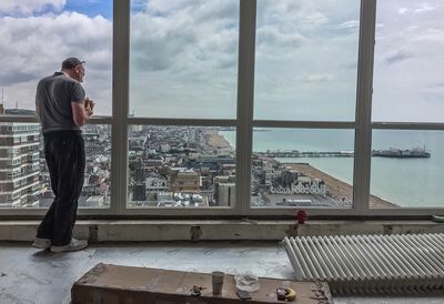 Rear view of man eating by window while standing in building