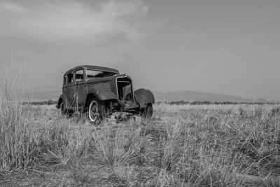 Abandoned car on field against sky