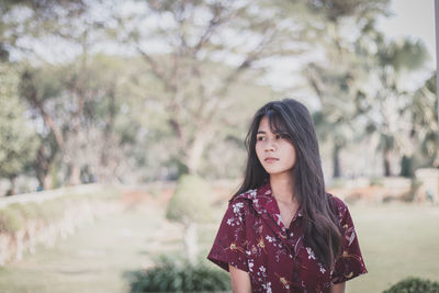 Beautiful young woman looking away while standing against trees