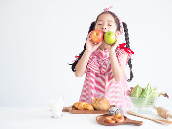 Girl with eyes closed holding apples against white background