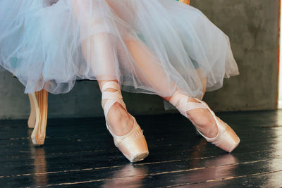 Low section of woman wearing ballet shoe while sitting on wooden floor