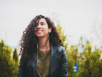 Young woman listening to music against sky