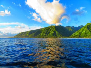 Scenic view of sea by mountain against sky