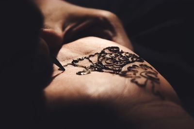 Cropped image of woman applying henna tattoo on hand in darkroom