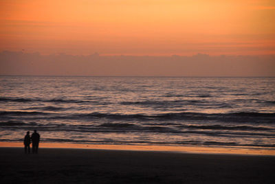 Silhouette man walking on beach against orange sky