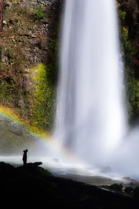 Silhouette of person at a waterfall with a rainbow