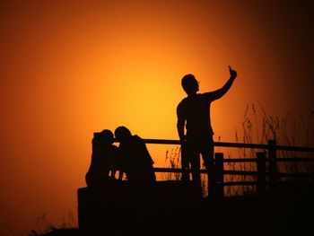 Silhouette people against orange sky during sunset