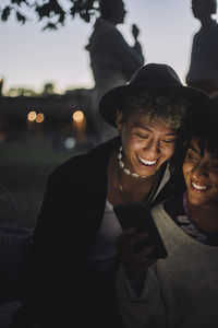 Happy transgender woman sharing mobile phone with male friend during sunset