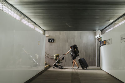 Woman with luggage and baby stroller walking in underground passage