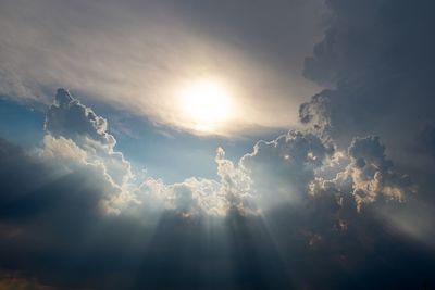 Low angle view of sunlight streaming through clouds