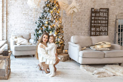 Cute girl toddler with her mom hugging at the decorated christmas tree in the house. happy family