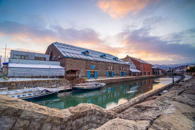 Buildings by canal against sky during sunset