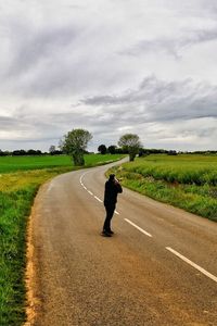 Man cycling on road amidst field against sky