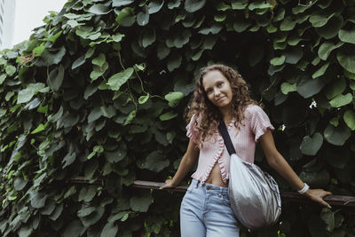 Young woman standing against plants