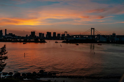 Silhouette city by sea against orange sky