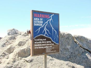 Close-up of information sign on beach against sky