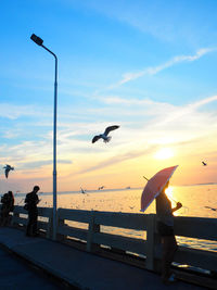 Silhouette woman standing by railing against sea during sunset