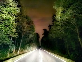 Country road amidst trees against sky