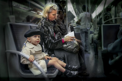 Thoughtful girl looking away while mother reading book in subway train