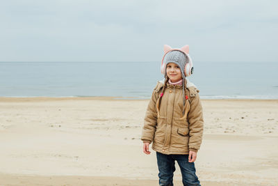 Little girl listens to music in children's pink headphones with cat ears and dances on the beach 