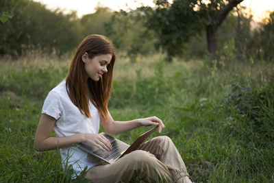 Young woman using mobile phone while sitting on field
