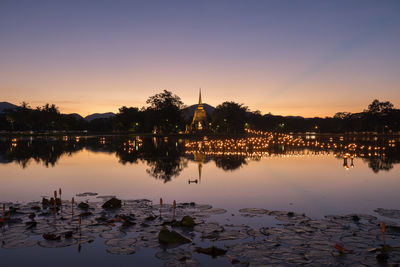 Scenic view of lake by silhouette buildings against sky during sunset