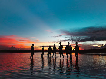 Silhouette men in lake against sky during sunset