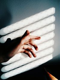 High angle view of sunlight falling on hand by wall