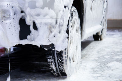 A car covered by soap foam while washing indoors - close-up low position view from back