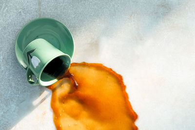 From above warm brown drink flowing from dropped green ceramic mug on saucer to gray table on cafe terrace