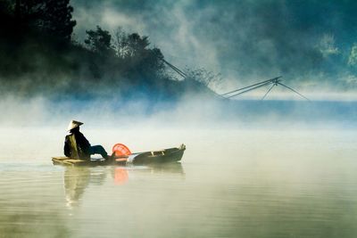 Man wearing asian style conical hat in boat on lake during foggy weather
