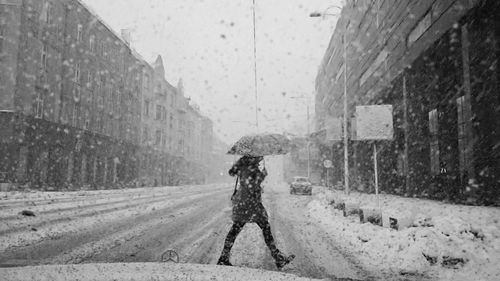 Side view of mid adult woman walking on road during snowfall seen through windshield