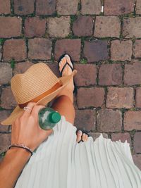 Low section of woman holding hat and bottle walking on walkway