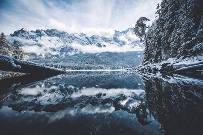 Scenic view of calm lake by snow covered mountains against sky